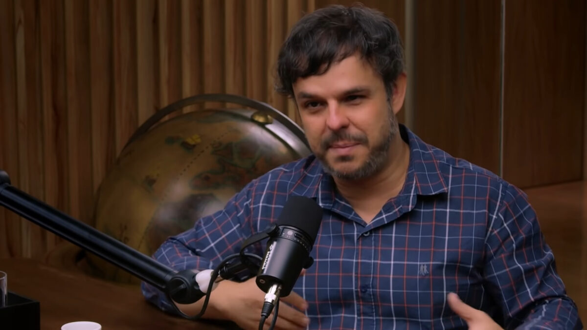 Adrilles Jorge sentando e com um microfone de rádio próximo a sua boca