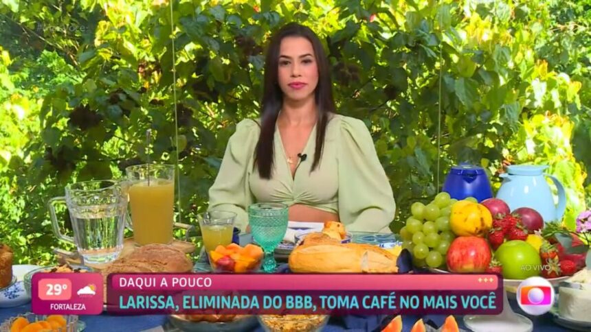 Larissa sentada de roupa verde com a mesa de café da manhã.