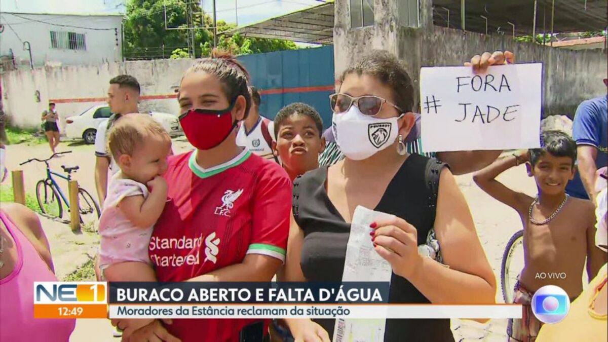Mulher com uma criança no colo e uma outra do lado segurando um papel e atrás dela um jovem com uma placa de Fora Jade.
