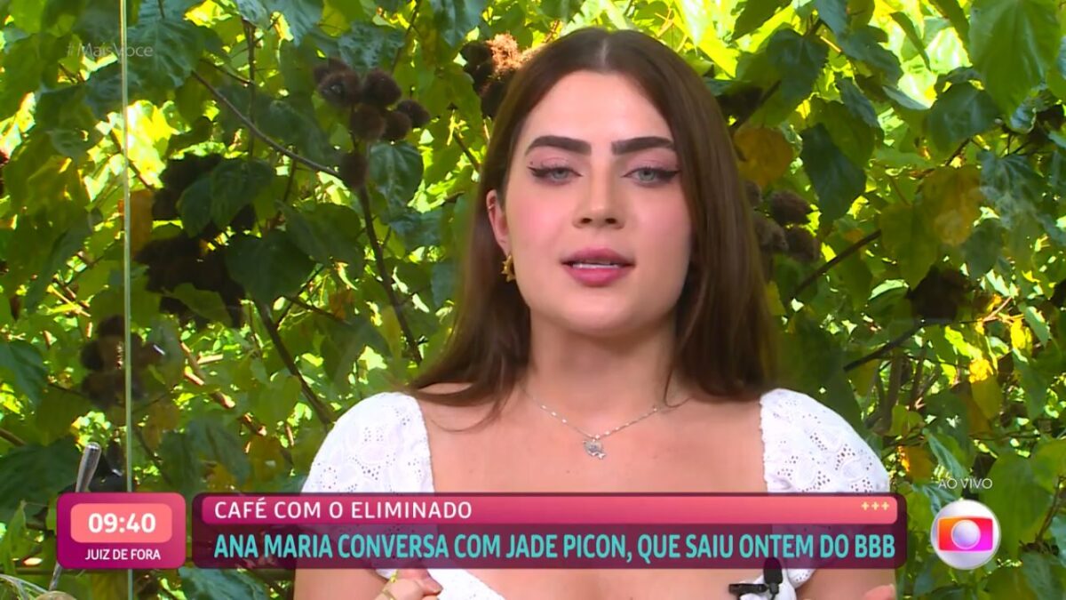 Jade com uma blusa branca sentada numa mesa.