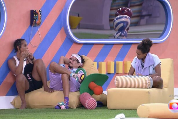 Linn da Quebrada sentada abaixo do Big Fone, ao lado dela Elizer e Jessilan sentada no sofá do BBB 22