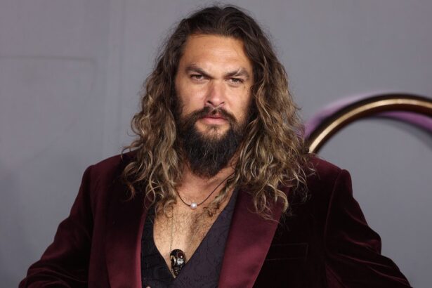 Jason Momoa vestido com um terno vinho e cabelo solto