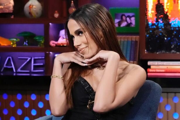 Anitta sentada em uma poltrona e fazendo um pose com as duas em baixo do queixo