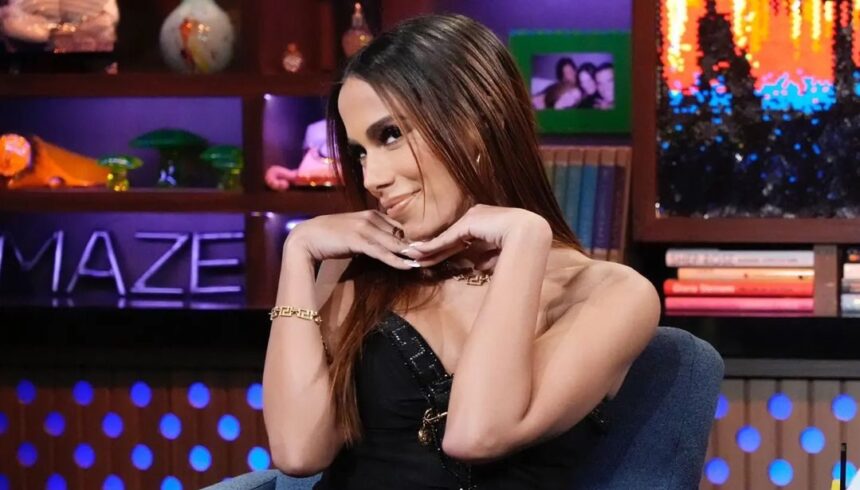 Anitta sentada em uma poltrona e fazendo um pose com as duas em baixo do queixo