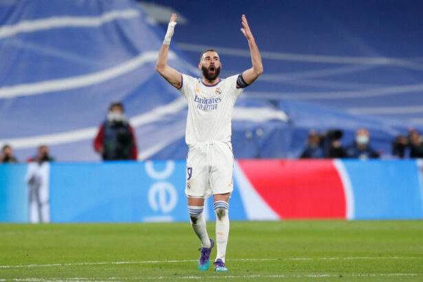 Benzema exaltado com os braços abertos em campo com a camisa do Real Madrid