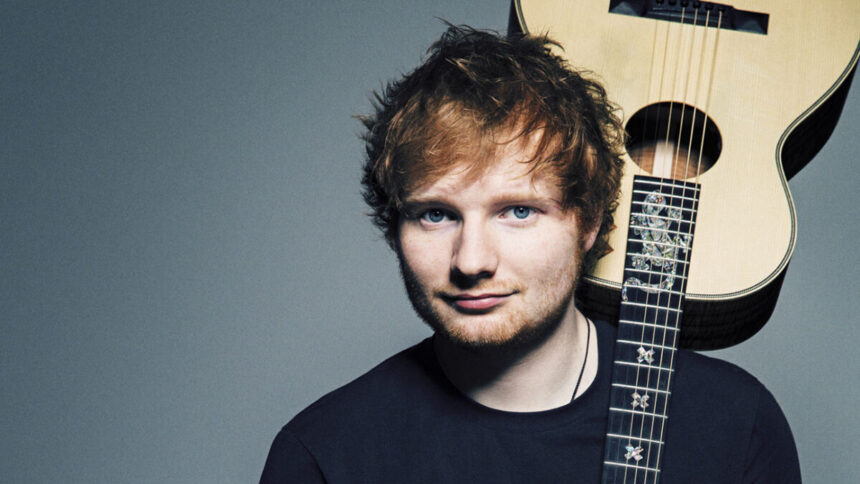 Ed Sheeran em uma foto posada, com um violão nas costas