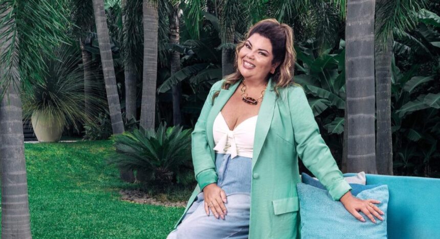 Fabiana Karla em foto posada, sentada na beira de um sofé e com um jardim ao fundo