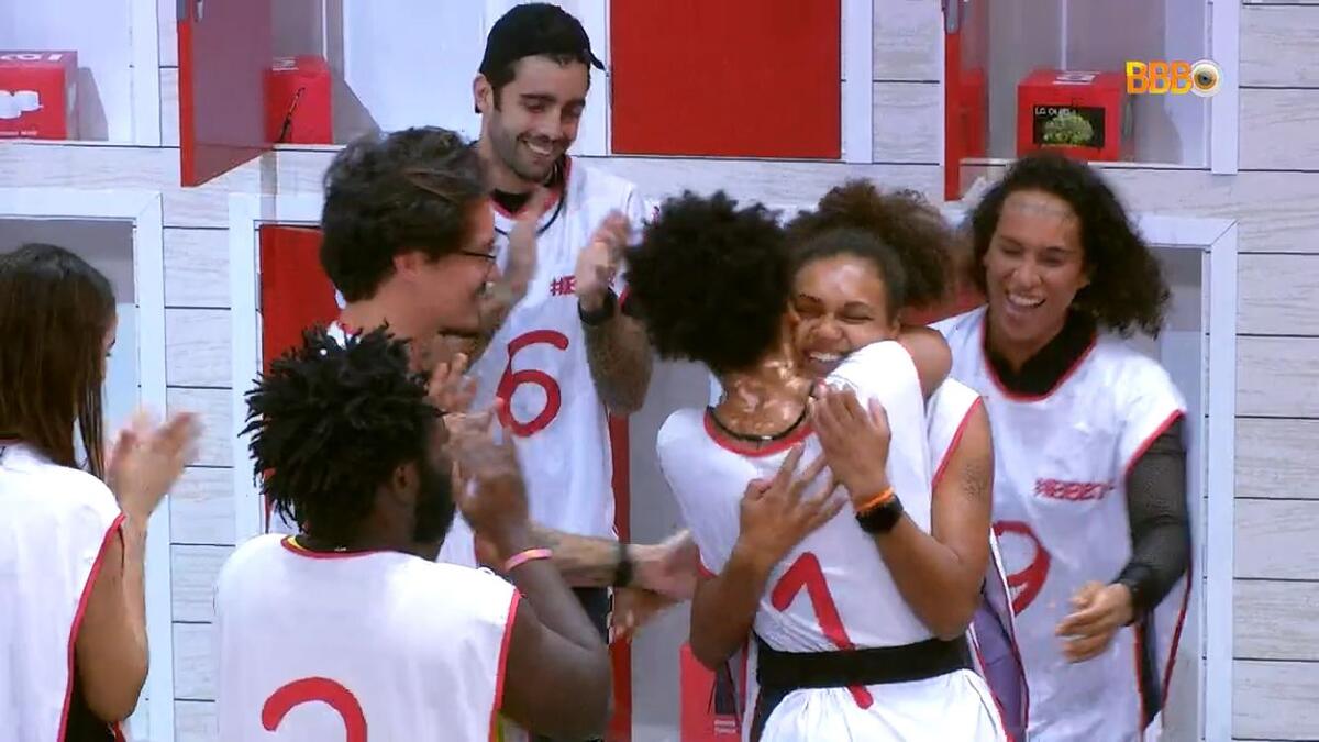 Jessi abraçada com Natália e os participantes comemorando.