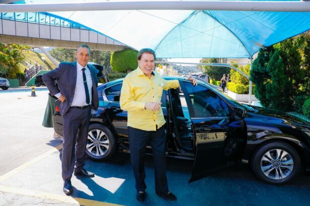 Silvio Sanos de blusa amarela saindo do carro na sede do SBT, com um segurança ao fundo