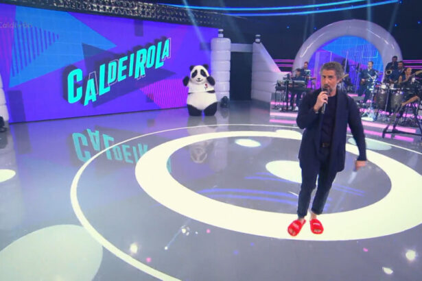 Marcos Mion no centro do palco do Caldeirão usando terno e pantufas laranjas