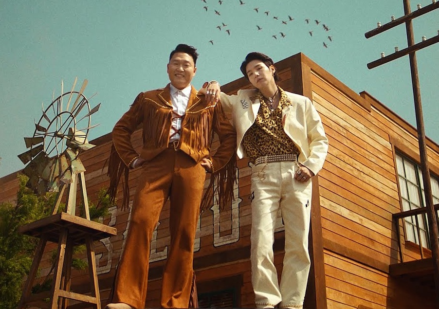 Psy e Suga abraçados em um cenário de faroeste