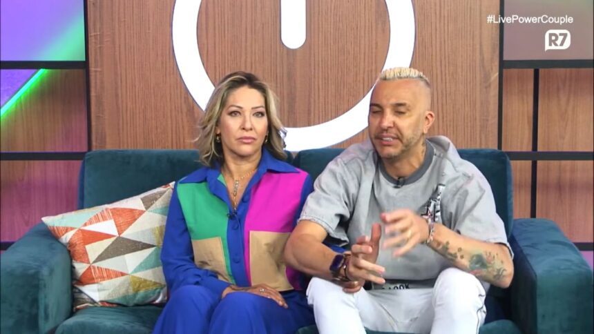 Baronesa e Rogério sentados no sofá em live do Power Couple