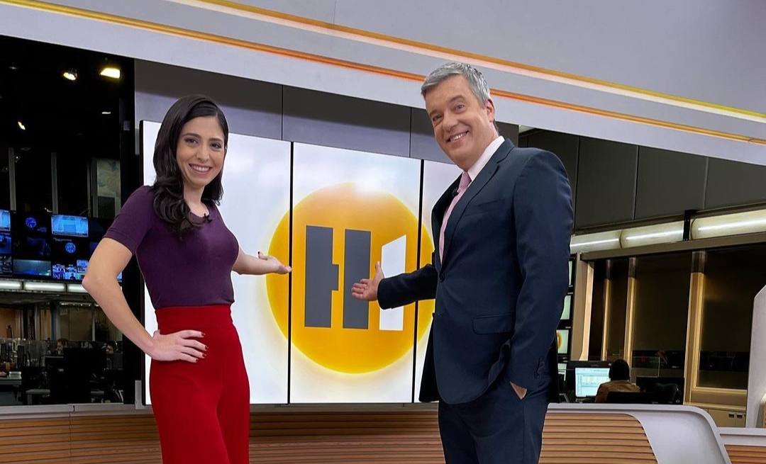 Cinthia Toledo ao lado de Roberto Kovalick nos estúdios do Hora e apontando pro telão