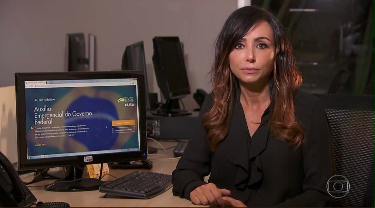 Elaine Bast em trecho de uma reportagem para o Jornal Nacional. Ela está sentada, ao lado de um computador de mesa