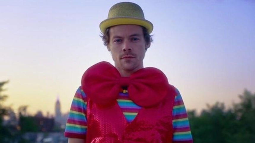 Harry Styles com um laço vermelho no pescoço e um chapéu amarelo na cabeça