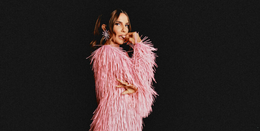 Ivete Sangalo em foto posada com uma roupa rosa em um fundo preto