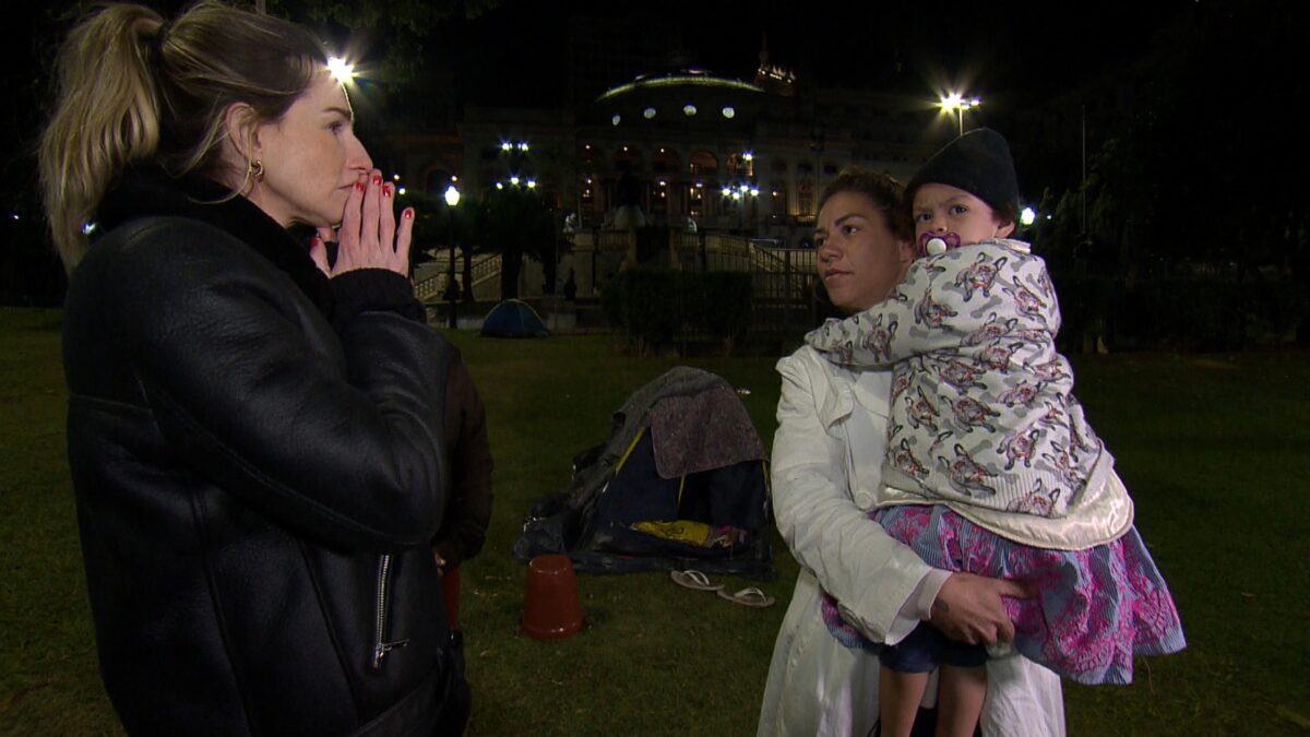 Mariana Weickert entrevistando uma mãe com uma criança de colo, em trecho de reportagem para o Domingo Espetacular