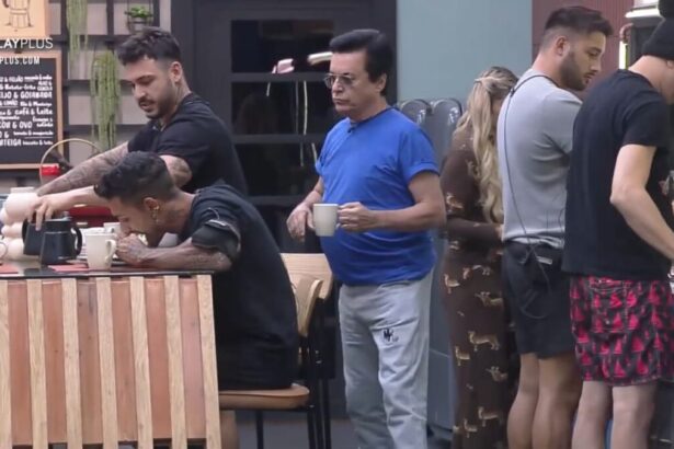 Nahim de camiseta azul atrás de Matheus que está sentado na mesa próximo de Hadad.