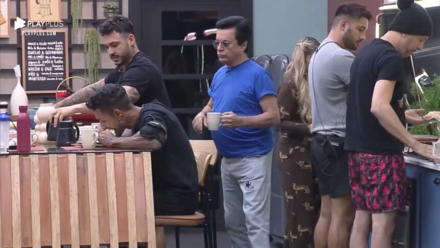 Nahim de camiseta azul atrás de Matheus que está sentado na mesa próximo de Hadad.