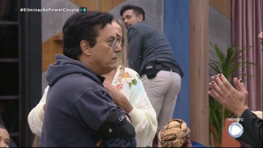 Nahim com semblante sério olhando para frente e Matheus atrás da imagem com as mão no joelho rebolando o bumbum.