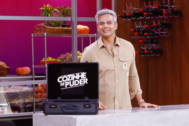 Otaviano Costa nos estúdios do Cozinhe de Puder, em uma foto posada. A frente dele, está uma maleta com o logo do programa