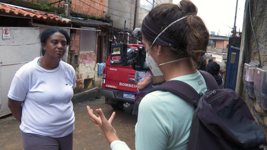 Repórter Nathalia Tavolieri entrevistando a dona Jussara, em meio ao barro da tragédia de Petrópolis