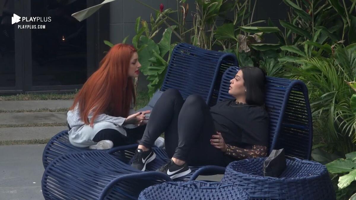 Brenda sentada de frente para Gabi na área externa.