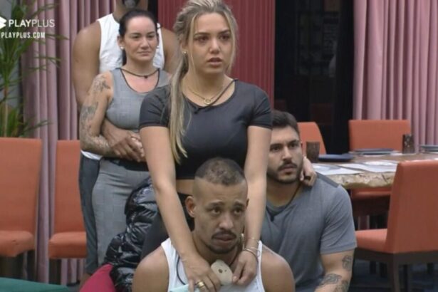 Karol em pé com cara de nervosa e Mussunzinho sentado próximo a esposa.