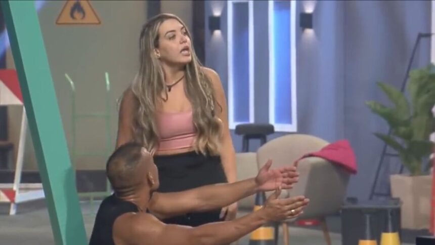 Karol de pé olhando para frente e Mussunzinho sentado olhando para a esposa com os braços apontados para frente.