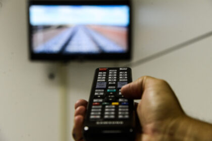 Mão segura um controle remoto em frente a TV