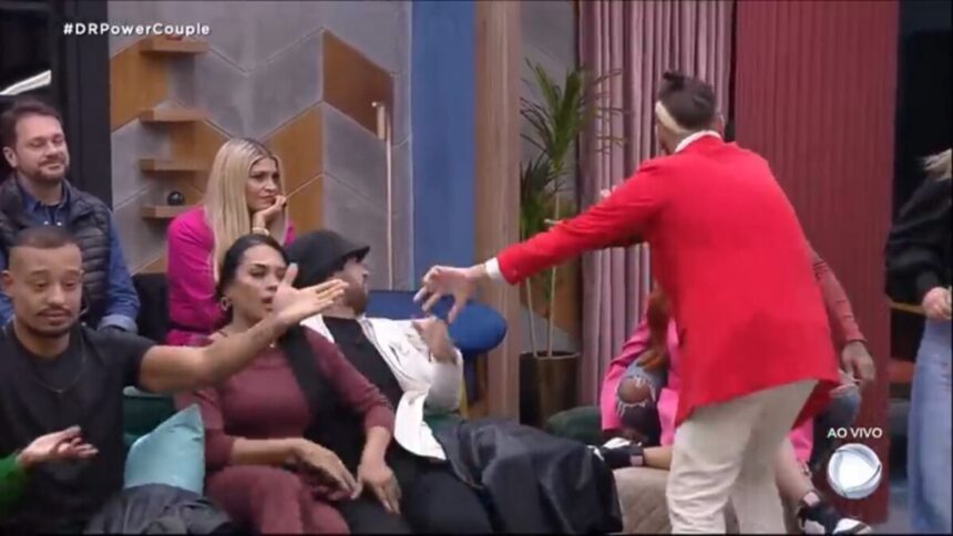 Participantes do Power Couple discutindo. Cartolouco em pé com uma roupa vermelha.