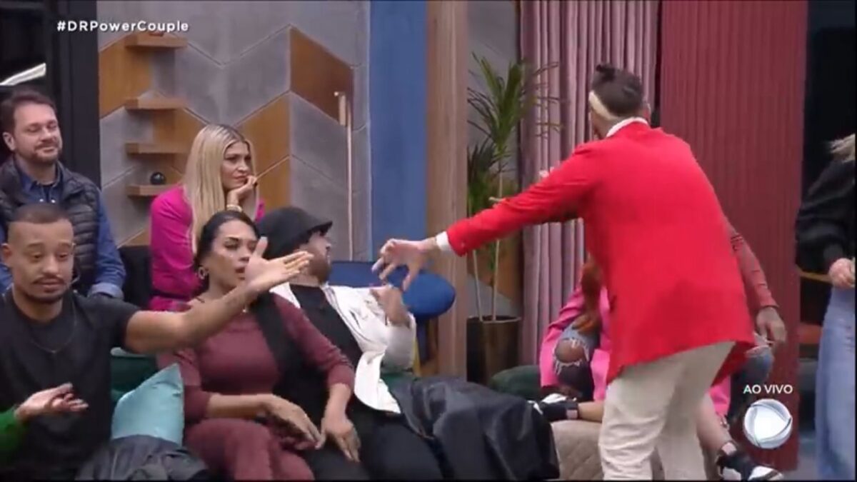 Participantes do Power Couple discutindo. Cartolouco em pé com uma roupa vermelha.