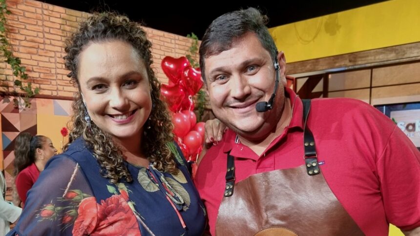 ApresentBianca Láua sorrindo ao lado do Padre Chef, ambos de vermelho e avental, na gravação do Sabor de Vida, da TV Aparecida