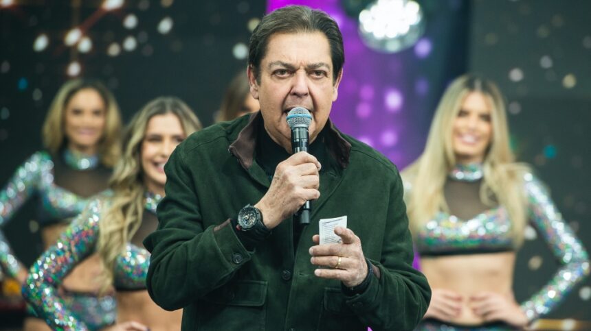 Fausto Silva com microfone e tabela na mão durante gravação do seu programa