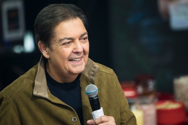 Apresentador Fausto Silva sorrindo, com jaqueta verde e camisa preta, segurando o microfone na gravação do seu programa na Band