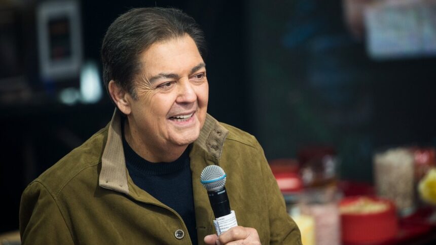 Apresentador Fausto Silva sorrindo, com jaqueta verde e camisa preta, segurando o microfone na gravação do seu programa na Band