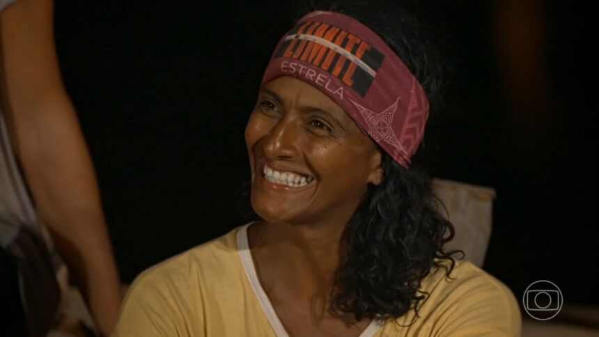 Flávia, de bandana roxa na testa, sorrindo, de camisa amarela, no portal de eliminação do No Limite