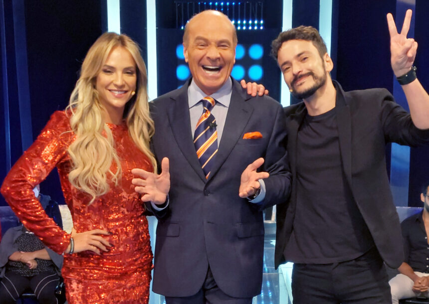 Gabi Martins de vestido vermelho, Marcelo de Carvalho de palito e gravata listrada laranja e preta e Fefito de preto sorrindo durante gravação