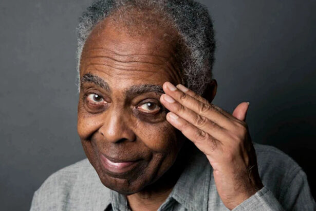 Cantor Gilberto Gil, de camisa cinza, com a mão na testa, fazendo continência