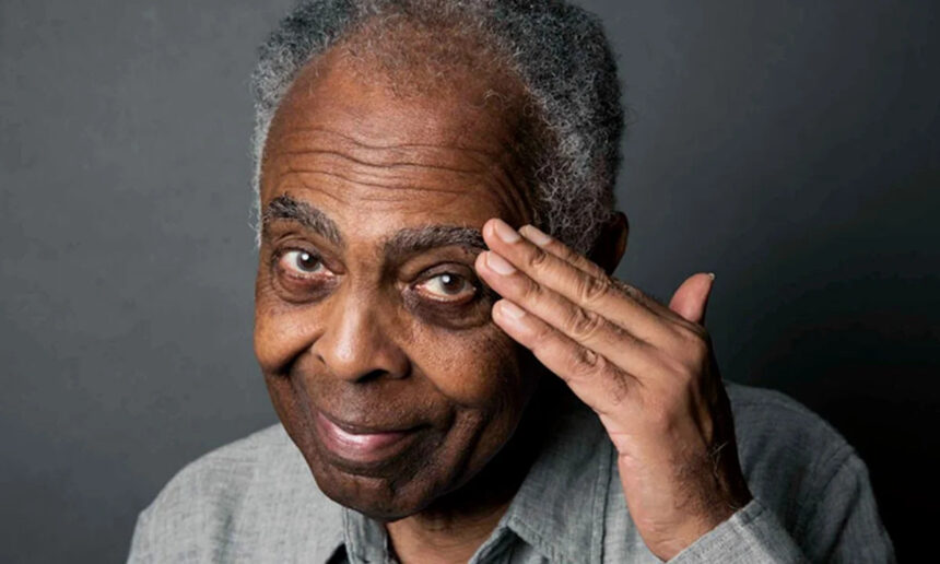 Cantor Gilberto Gil, de camisa cinza, com a mão na testa, fazendo continência