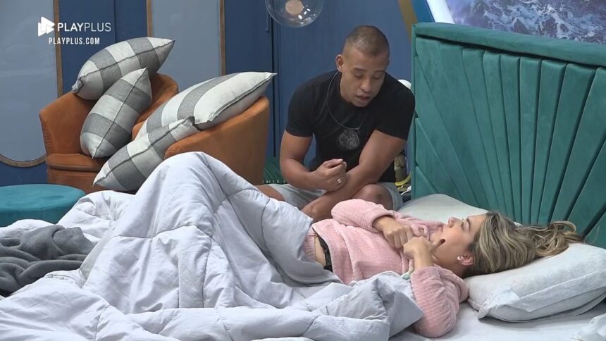 Karol deitada na cama toda enrolada de frente para o Mussunzinho que estava sentado.