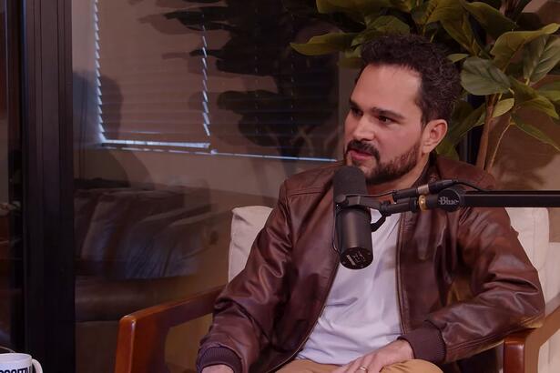 Luciano Camargo em trecho da entrevista para o podcast, com um microfone de rádio próximo ao seu rosto