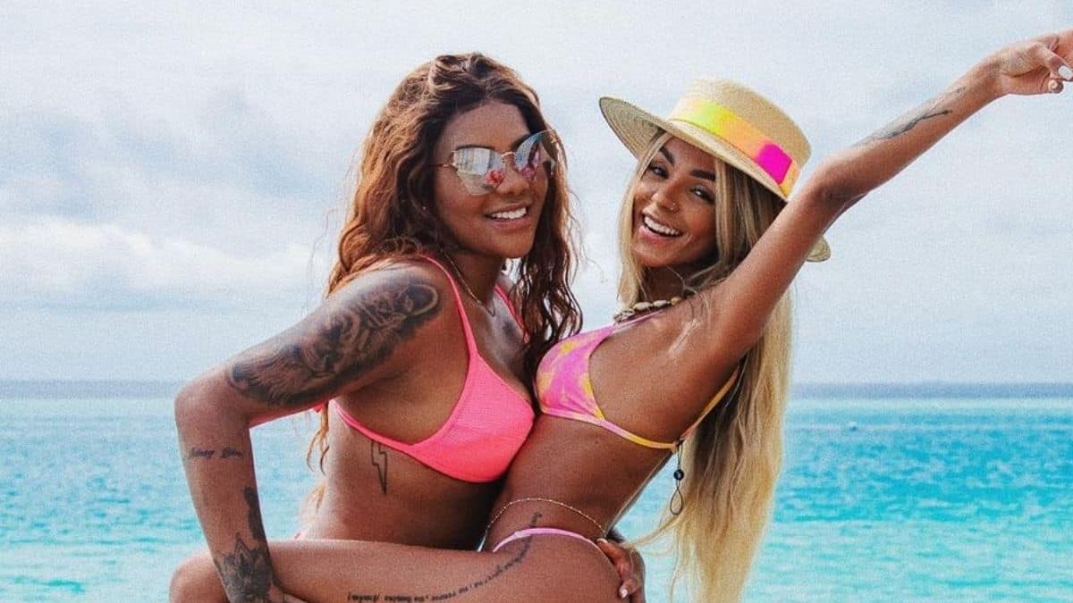 Ludmilla de biquine rosa, de óculos, com a mão na coxa de Brunna, que está de chapéu com os braços pra cima, em Maldivas