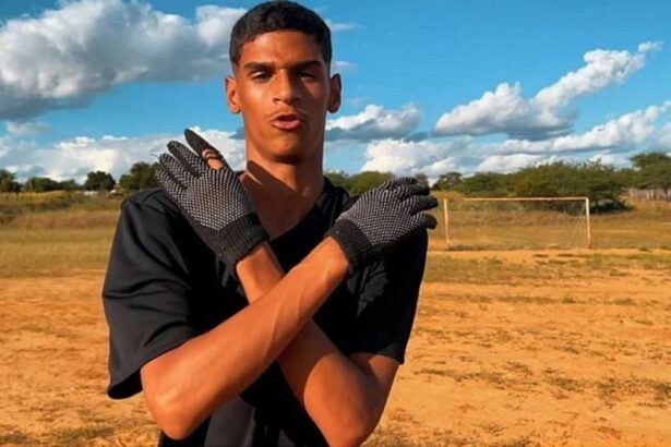 Iran Ferreira, o Luva de Pedreiro, com os braços abraçados no corpo, na pose do "Receba!" em um campo de terrão