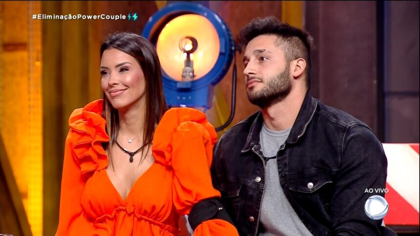 Ivy sorrindo ao lado de Nandinho no cenário de eliminação do Power Couple Brasil 6