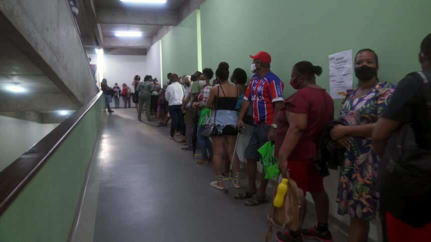 Pacientes em uma filha de hospital, encostado em uma parede, em trecho do Profissão Repórter sobre cirurgia bariátrica