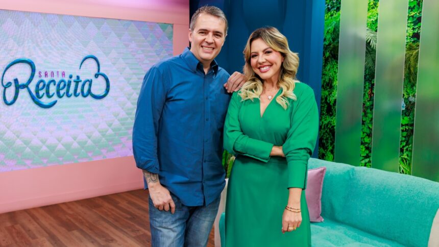 Apresentadores Abiane Souza (vestido verde, cabelo solto, sorrindo) ao lado de Leonardo Roncon (camisa azul e calça jeans, sorrindo) durante gravação do Santa Receita, da TV Aparecida