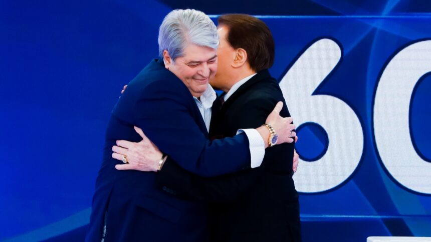 Datena de palitó e gravata, sorrindo, dando um abraço em Silvio Santos no Programa Silvio Santos, do SBT