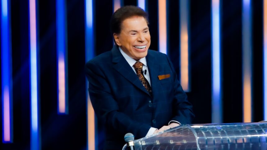 Silvio Santos sorrindo, de palitó e gravata na bancada do Troféu Imprensa, do SBT