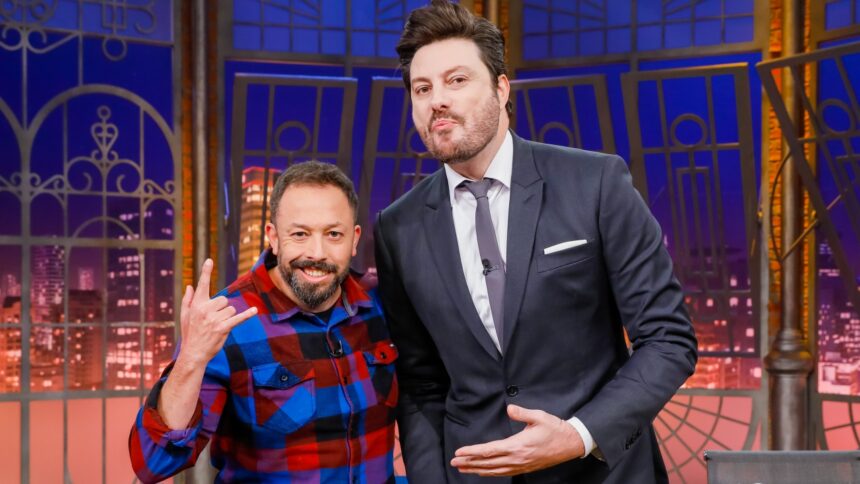 Fabio Gueré sorrindo, de camisa quadriculada azul e vermelha, fazendo símbolo do rock in roll com a mão direita ao lado de Danilo Gentili, que está de palitó e gravata, apontando para o humorista